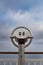 Close up of a fixed telescope at a vantage point against a cloudy sky