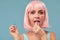 Close up of a flirtatious female model on blue background wearing a pink wig with a candy in mouth. Pretty glamorous