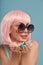 Close up of a flirtatious female model on blue background wearing a pink wig holding different kinds of candies. Pretty