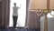 Close-up of floor lamp standing in hotel room with blurred Caucasian maid opening curtains at the background. Wide shot