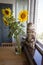 Close-up fluffy kitten Maine Coon sitting on the windowsill next to a vase of sunflowers on the kitchen table