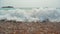 Close up of foamy waves crashing on beach stones, beatiful pebbles