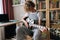 Close-up of focused curly preteen girl sitting on chair and playing on electric guitar, learning new song at home.