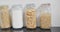 Close up of food storage jars with flour and various kinds of pasta on shelf in kitchen, slow motion