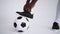 Close-up of the foot of a professional black football player standing on the ball in slow motion in the white background