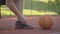 Close-up foot of unrecognizable basketball player tying shoelaces on sneakers. Ball lying in sunlight on outdoor court