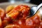 Close-up of a fork twirling a single ravioli pasta coated in a rich tomato sauce