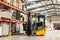 Close up of forklift working in warehouse. Industrial lift truck, jitney lifting and moving materials in factory.
