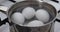 Close-up of four white eggs in clean transparent boiling water on a gas stove