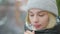 Close-up of freezed Caucasian young woman in warm hat and coat blowing in hands warming up. Portrait of beautiful slim