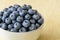 Close up of fresh blueberries in a white ceramic bowl on a yellow crackle background