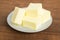 Close-up of fresh butter pieces on a white plate. Plate with butter on a brown wooden background. Sandwich butter. Natural fat