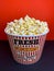 Close up fresh buttery popcorn in a stripped red and white bowl on red background