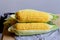 Close up of fresh corn cobs with leaves on a wooden table over grey wall background. Raw corncobs on light brown wooden table,