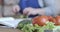 Close-up of fresh organic vegetables lying on the table as blurred female hands cutting cucumber at the background