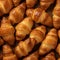 Close-up of freshly baked tasty croissants as background, placed in rows on a black tray. Food concept. Warm Fresh Buttery