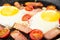 Close up of fried eggs with gammon and tomato in frying pan