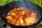 Close-up of fried pieces of pork ribs in a black cast-iron cauldron. Food in nature. Small depth of field