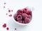 Close up of frozen rasberries in a white bowl on a white background with selective focus.