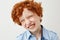 Close up of funny red haired boy with freckles smiling with closed eyes, making silly faces when mother tries to make