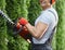 Close up of gardener in overalls trimming hedge outdoors