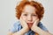 Close up of ginger little boy with freckles and curly hair, holding head with both hands looking in camera with funny