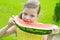 Close-up of a girl biting a large slice of ripe watermelon against a green lawn