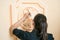 Close up of a girl (dark hair and black clothes) decorating a wall with a floral motive element with a brush