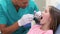 Close up of girl keeping mouth open while dental assistant examining her teeth