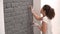 Close-up of a girl painting a brick wall in gray using a paint brush