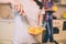 Close up of girl`s hand blending eggs with special equipment in glass bowl. Guy stands behind her and holds yellow cup.