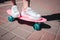 Close up of girl`s legs and feet wears white sneakers. Girl is standin on pink skate with both feet. There is a sunny