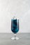 Close-up glass of blue lagoon cocktail. Tall glass of refreshing drink on light grey background. Vertical orientation, copy space