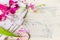 Close up of glass bottle of lotion with pink orchid flowers on white towel on light wooden background, top view