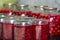 Close-up of glass jars with ripe red juicy sweet cherries covered with metal lids upside down on wooden plate. Homemade preserved