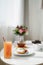 Close-up of a glass with juice and a drinking straw on a table with breakfast and a bouquet of flowers on a blurred