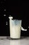 Close-up of glass of milk, with liquid falling, on white marble table, black background, vertically,