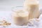 Close-up glass of oat milk and flakes on white linen napkin on white table.