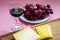 Close-up of glass of red wine, sliced yellow cheese Edam on brown wooden cutting board and sweet red grapes on white plate. Still