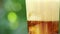 Close-up of a glass with a refreshing cold drink with pieces of ice and bubbling liquid on a blurry summer foliage