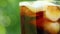 Close-up of a glass with a refreshing cold drink with pieces of ice and bubbling liquid on a blurry summer foliage