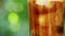 Close-up of a glass with a refreshing cold drink with pieces of ice and bubbling liquid on a blurry summer foliage