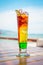 Close up of glass with refreshing layered cocktail with lime on table on beach.