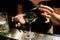 Close-up of glass in which female bartenders hand adds ingredient