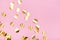 Close up of gold metallic confetti on pastel pink background.