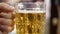 Close up of golden bubbling beer in a cup holding by one hand ready to drink it up with blurry background of people in a party