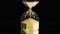 Close-up of golden hourglass on black background. Stock footage. Golden grains in hourglass had completely crumbled