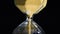 Close-up of golden hourglass. Stock footage. Stylish hexagon hourglass with falling gold specks on black isolated