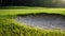 Close-up of a golf course bunker with lush green grass around it, showcasing the contrasting textures and the background green