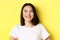 Close up of good-looking asian woman in white t-shirt, smiling and glancing left with pleased face, standing over yellow